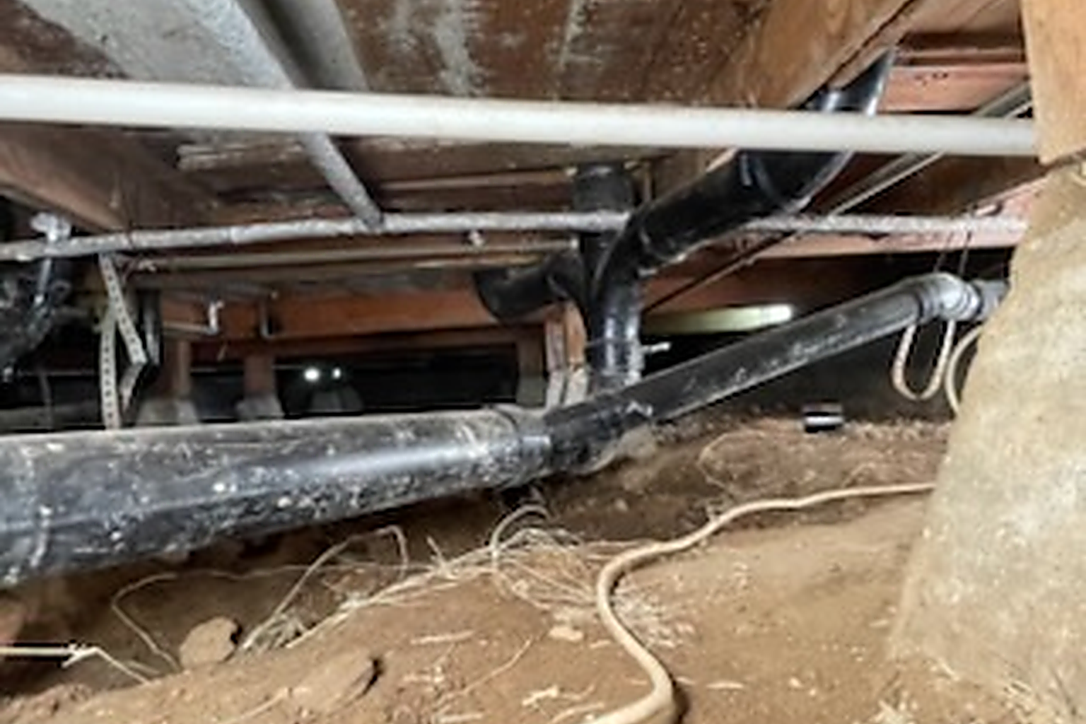 Supply and drain lines running through the crawlspace under a house, the supply run strapped up against the floor joists