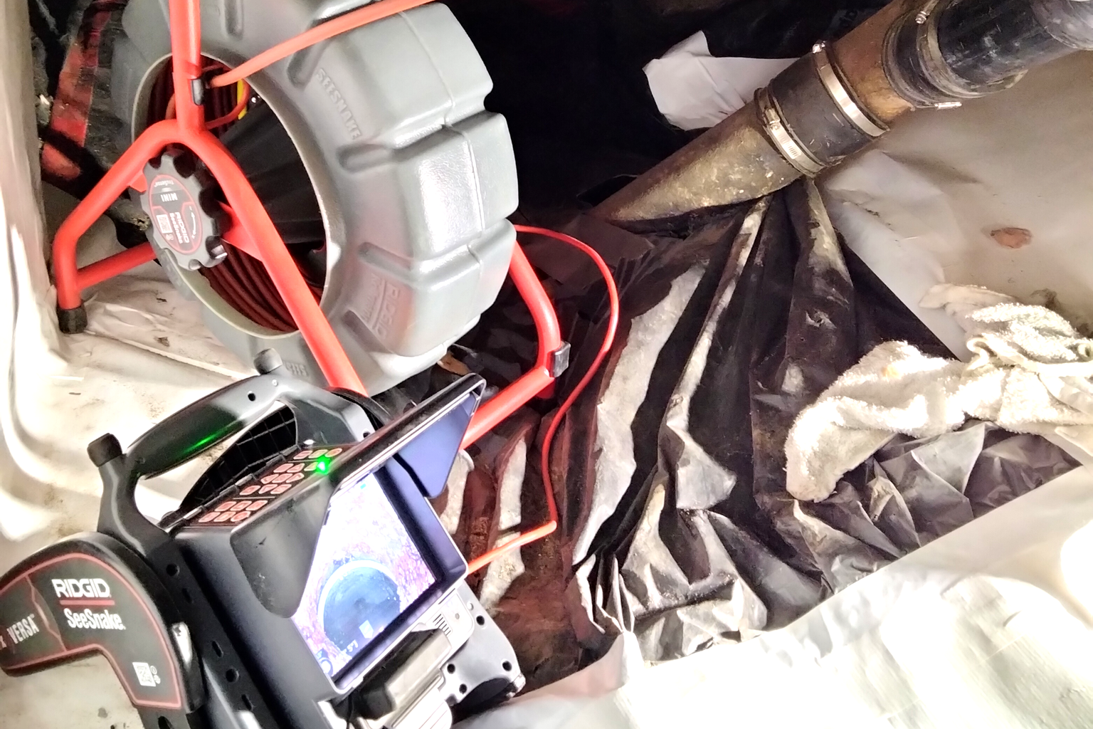 A RIDGID SeeSnake sewer camera reel and its monitor set up in the back of the van, with the camera line coiled and drain hose alongside