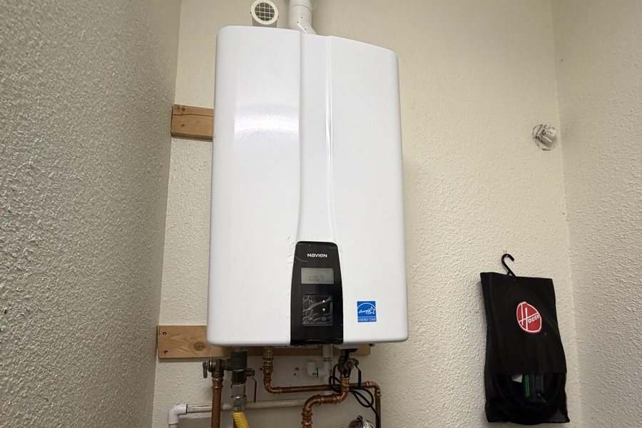 A Navien tankless mounted on a wood backer in a Sacramento utility closet, its copper manifold and service valves below