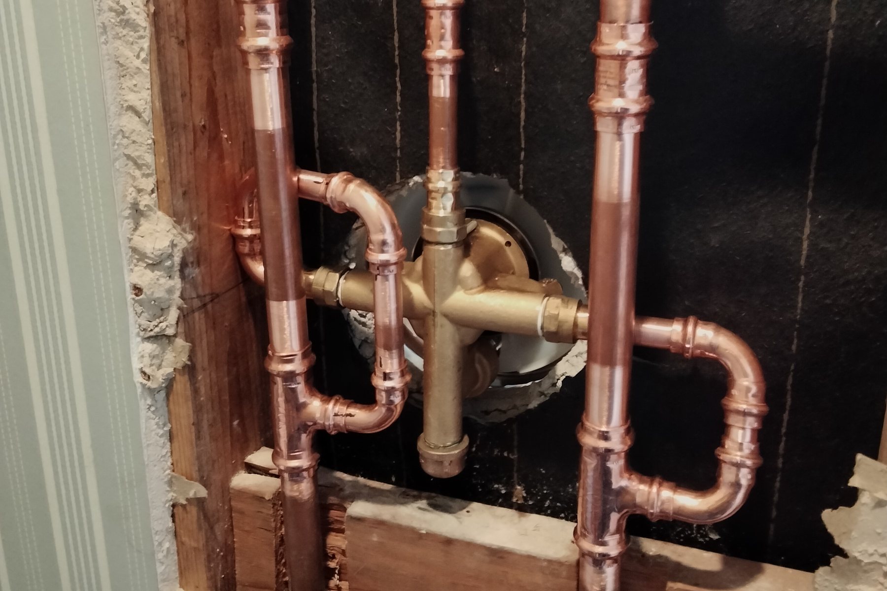 An opened bathroom wall with a brass tub and shower mixing valve roughed in on new copper, elbows sweated and risers run between the studs