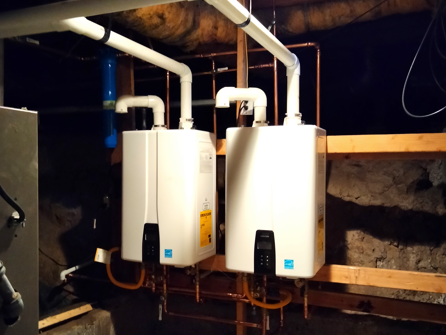 Two Navien tankless units mounted side by side in a cascade beneath a Sacramento home, vents run overhead and copper supply and gas lines dropping below