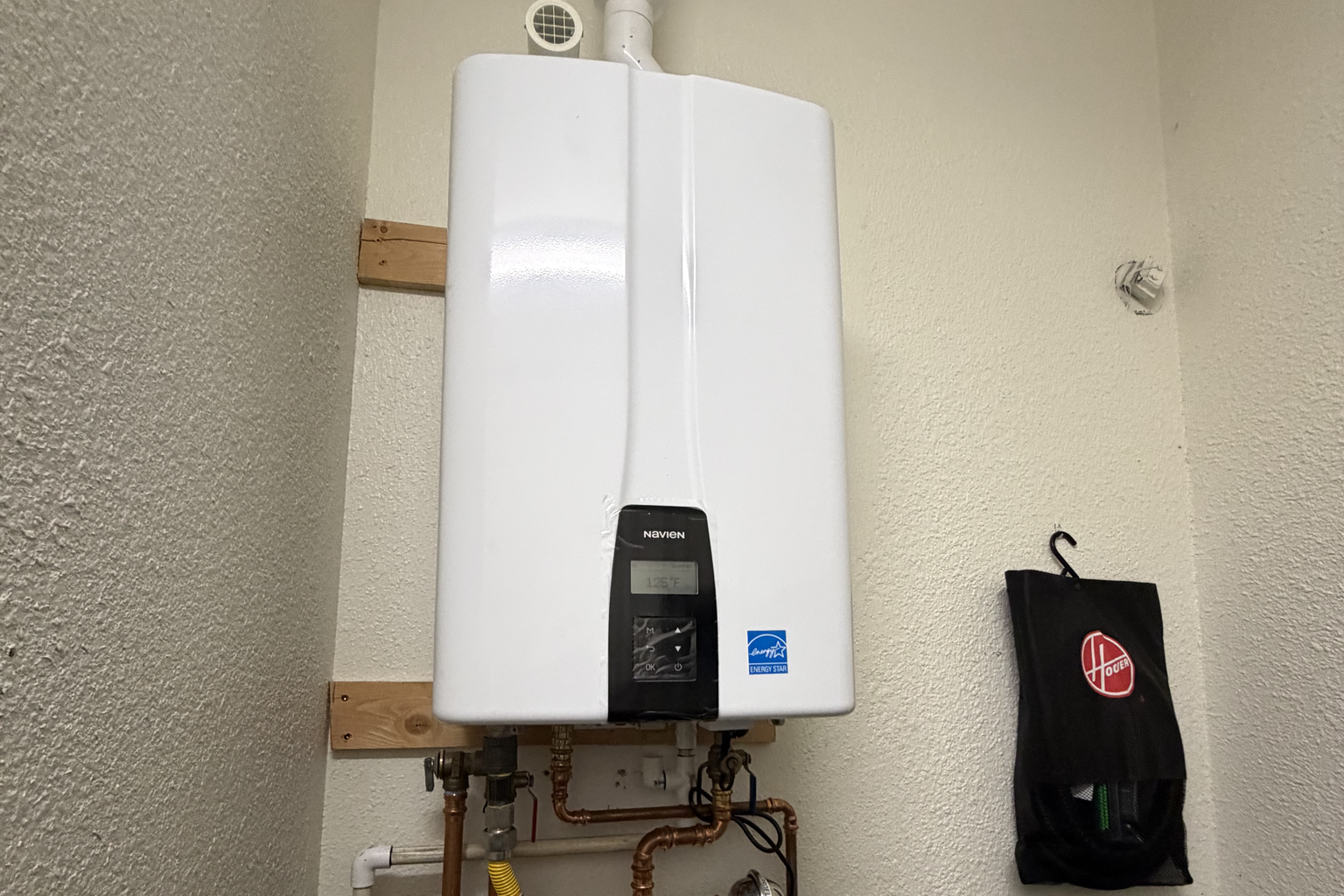 A Navien tankless mounted on a wood backer in a Sacramento utility closet, vent out the top and copper supply, gas and service valves run below
